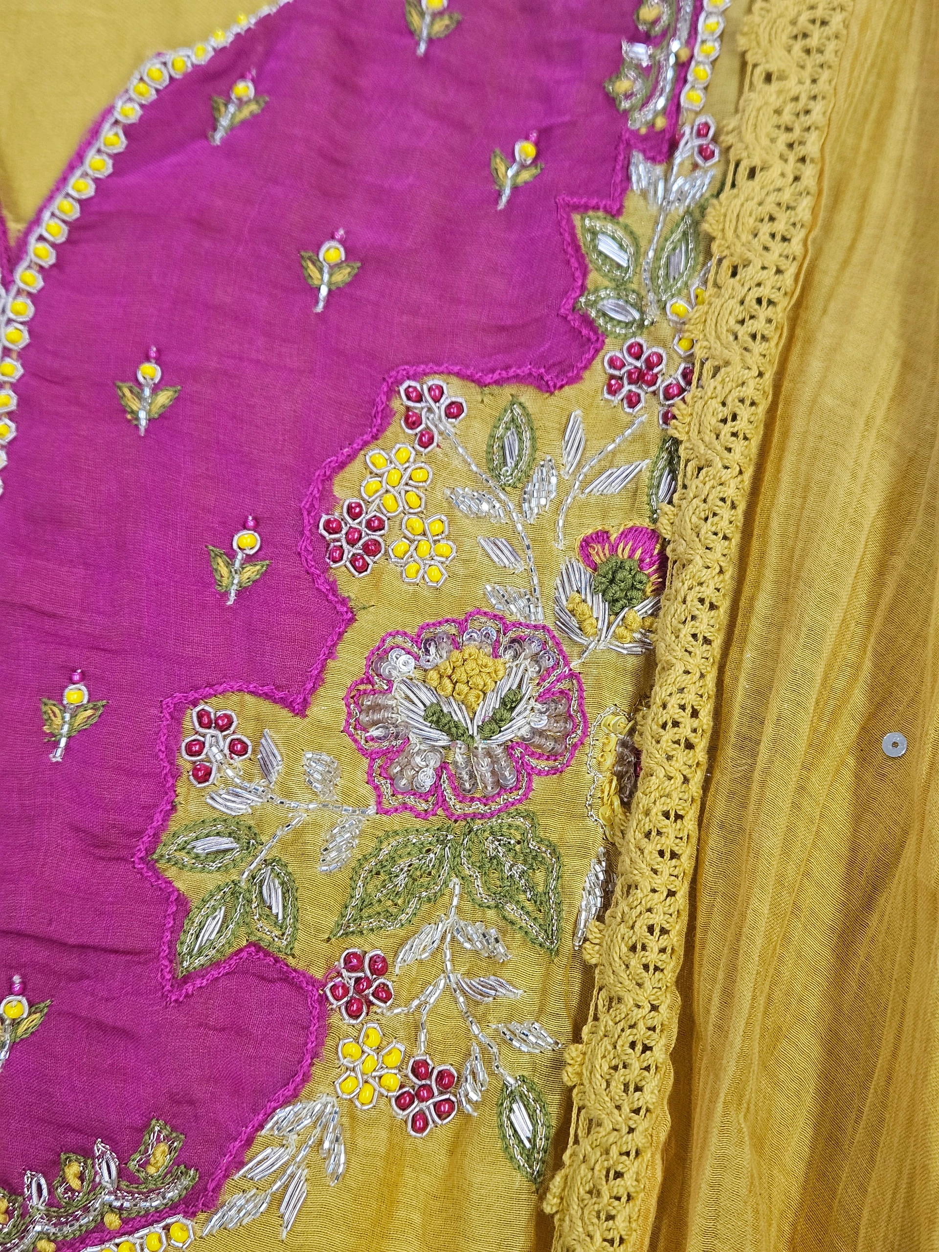 Mustard yellow Chanderi silk suit with intricate floral embroidery in pink, green, and yellow hues, featuring a lace border. Perfect for festive and wedding wear.