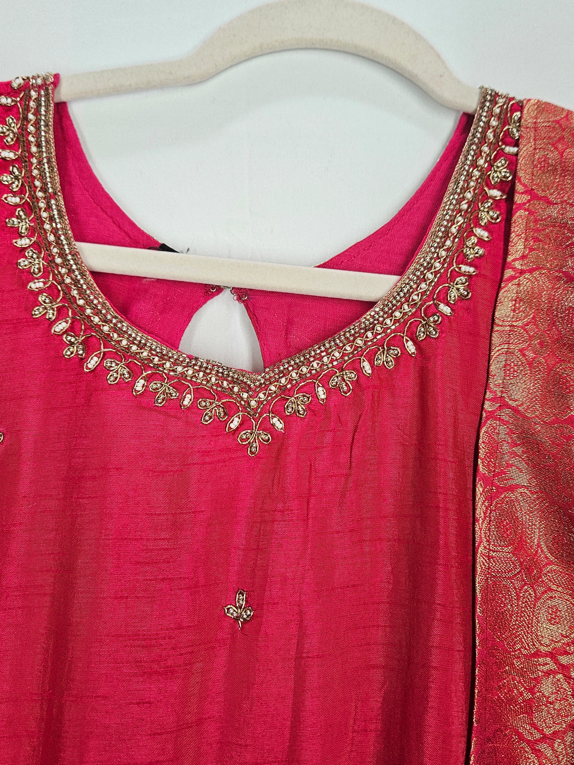 Pure Dola Silk ethnic dress in vibrant pink with intricate gold embroidery on the neckline and a rich brocade dupatta, perfect for weddings and festive occasions.