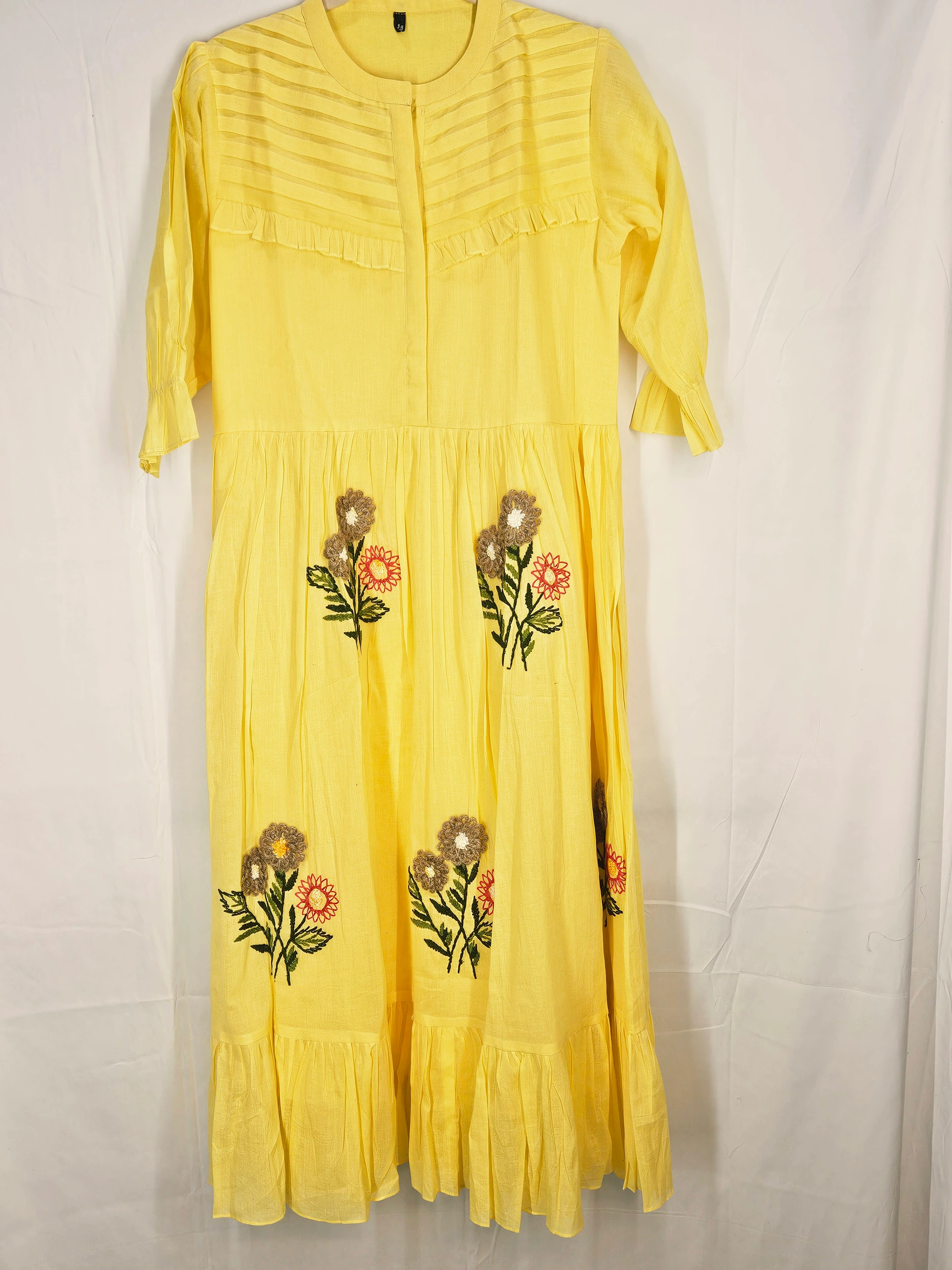 Yellow mul cotton ethnic dress with three-quarter sleeves, pleated yoke, and floral embroidery in vibrant colors, perfect for festive occasions.
