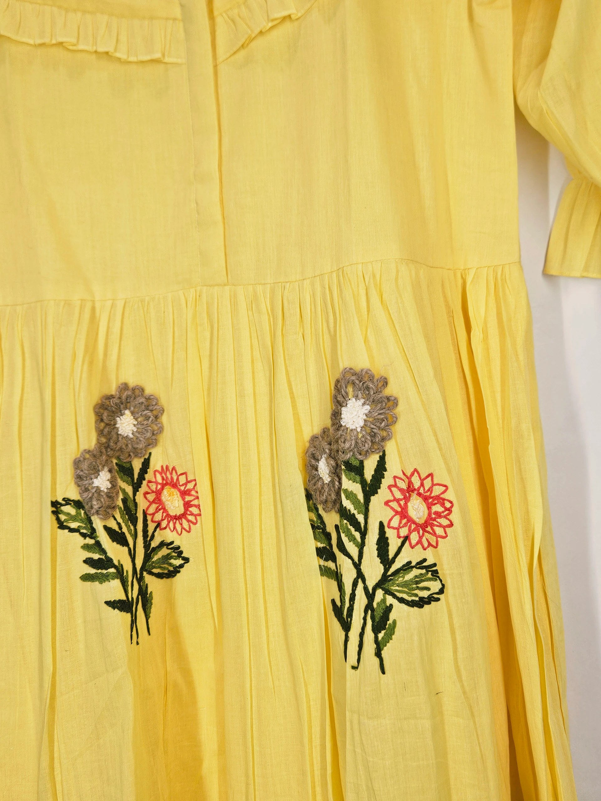 Yellow mul cotton ethnic dress with floral embroidery in red, white, and green on the skirt, perfect for festive occasions.