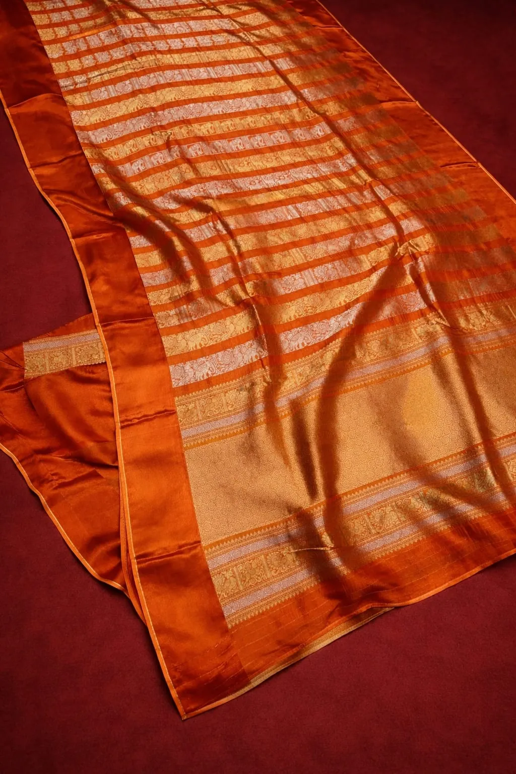 Luxurious pure Russian crape saree in rich orange with intricate gold stripes and border, perfect for elegant ethnic occasions.