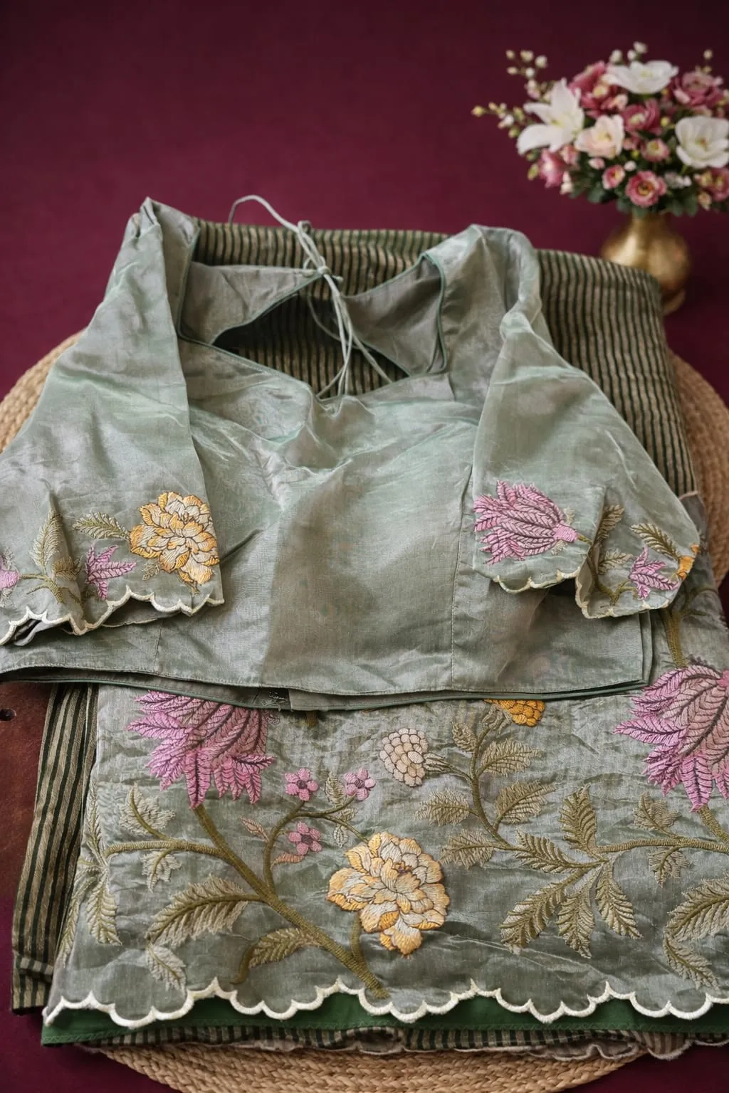Elegant Banarasi Kora tissue saree in sage green with floral embroidery in pink and yellow, paired with matching blouse.