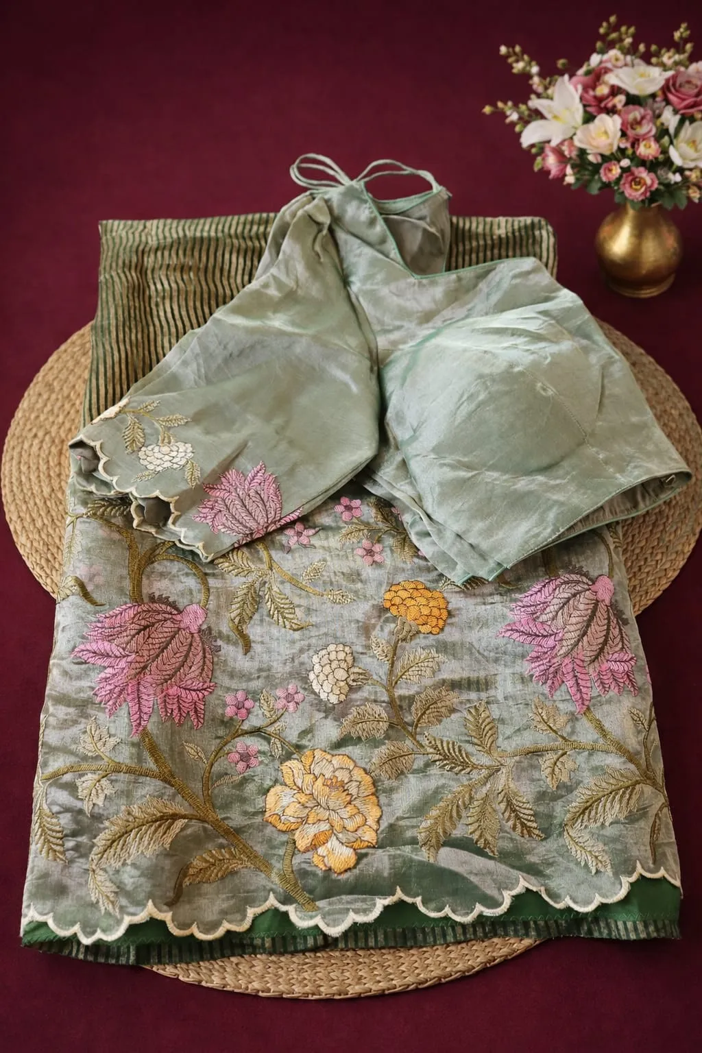 Elegant Banarasi Kora tissue saree in sage green with floral embroidery in pink, yellow, and white, paired with blouse.