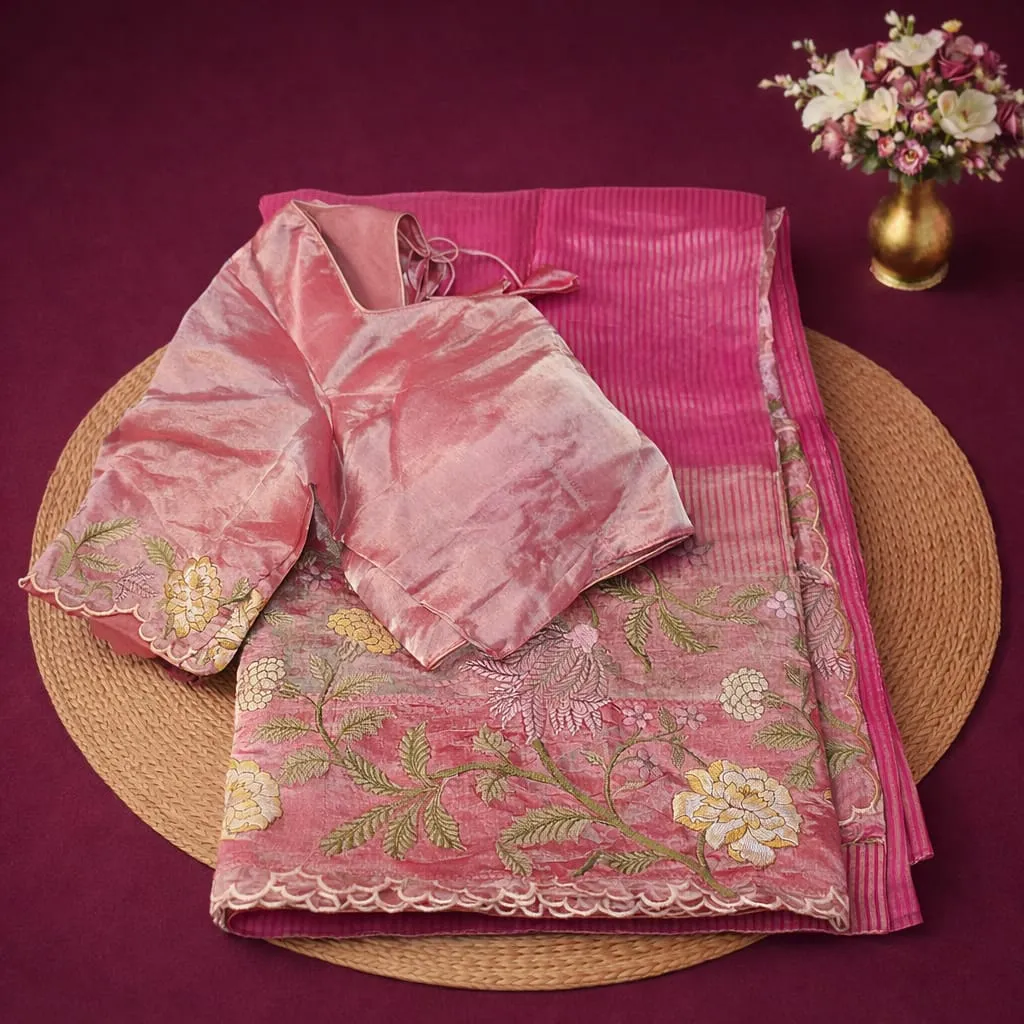 Elegant pink Banarasi Kora tissue saree with floral embroidery and matching blouse, displayed on a mat with flowers.